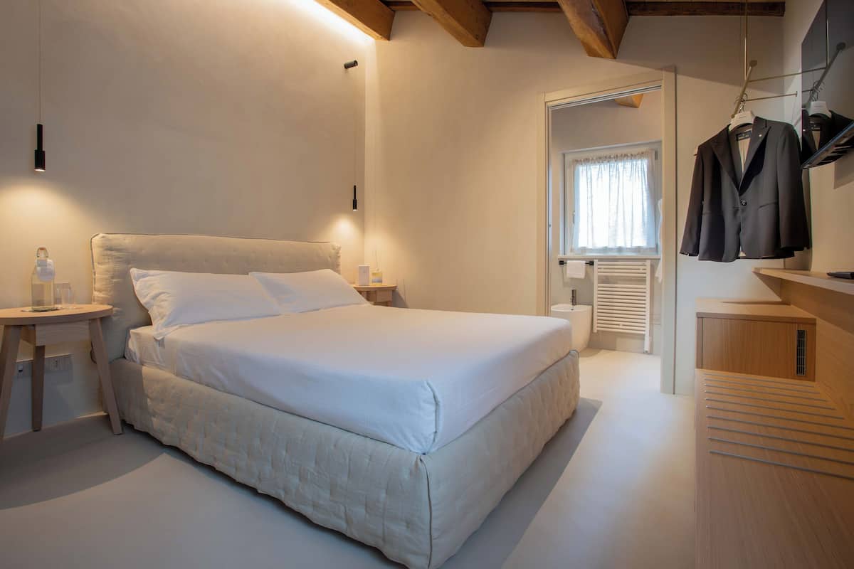 Un dormitorio ordenado con una cama grande, mesitas de noche, un perchero y una ventana con cortinas.