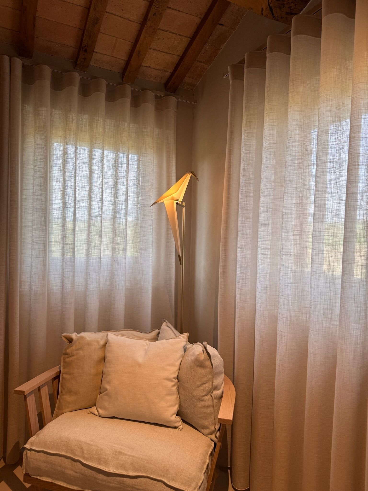 A cozy room with a bed, a floor lamp, and sheer curtains.