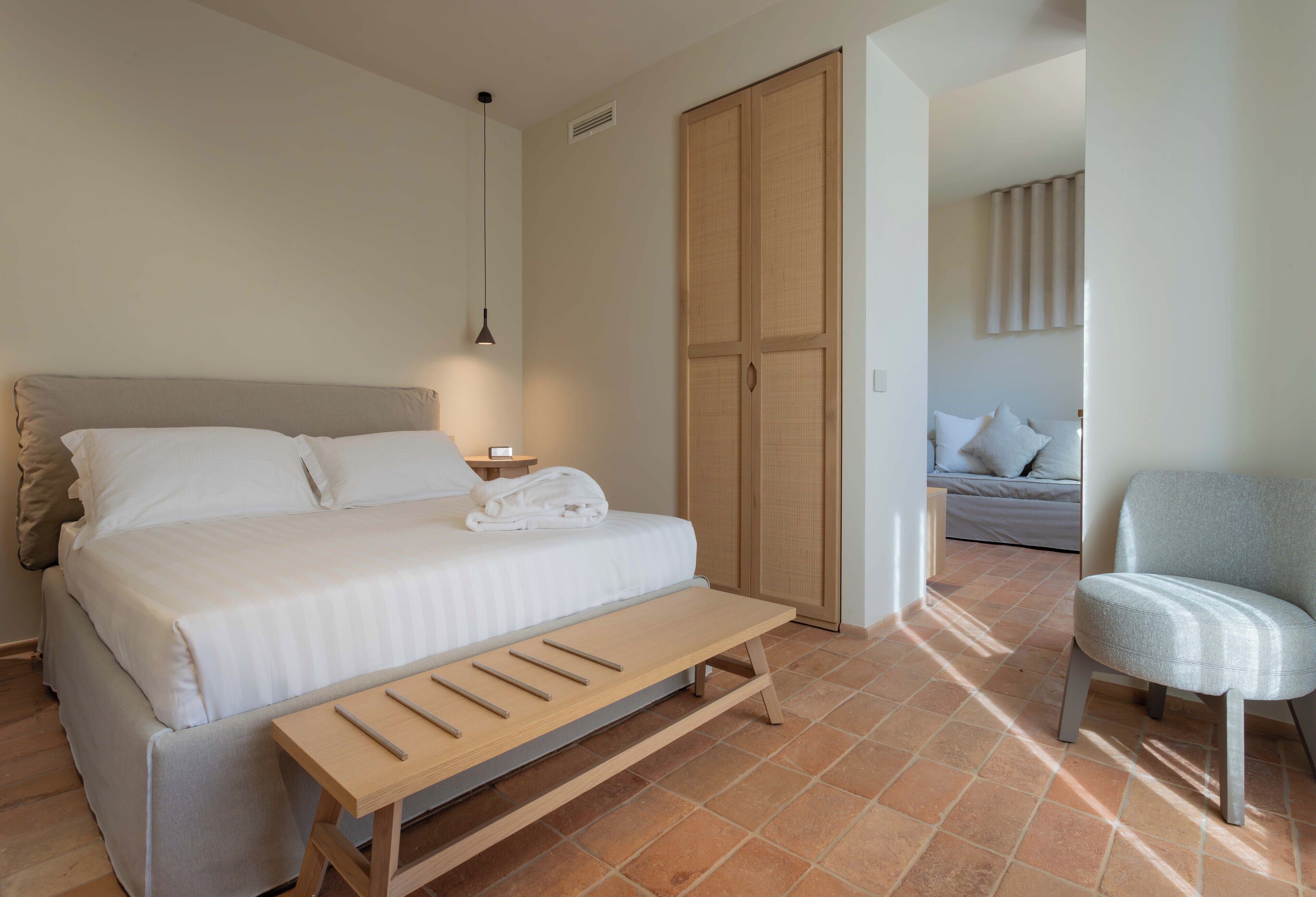 Ein Schlafzimmer mit Bett, Nachttisch, Bank, Kleiderschrank und Stuhl.