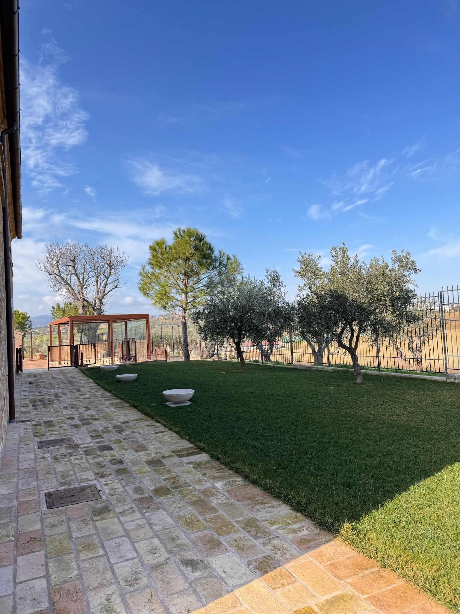 Eine Terrasse mit Steinplatten, einer Glasveranda und einem Rasen mit Bäumen.
