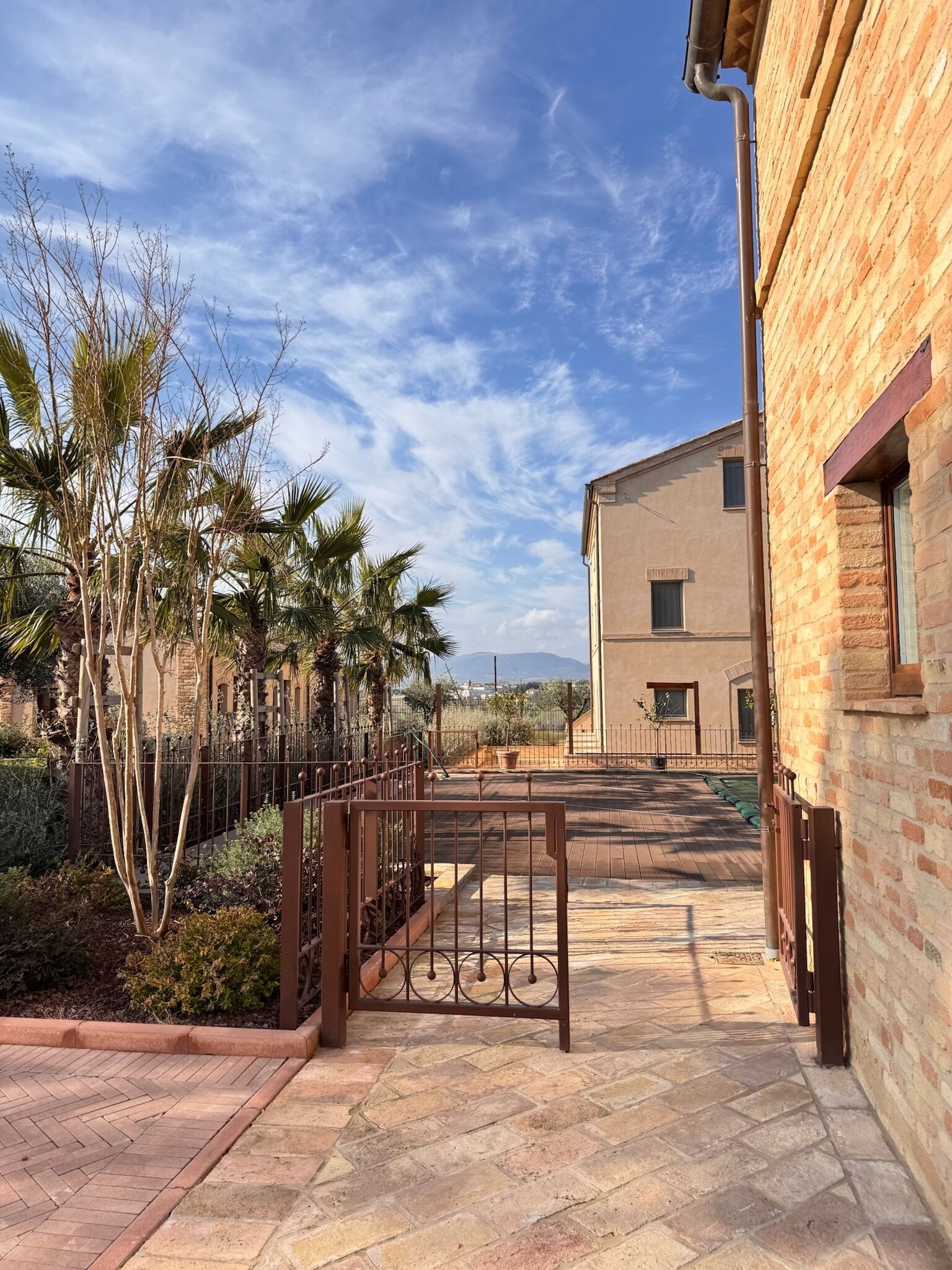 Un patio con sendero adoquinado, palmeras y un edificio de ladrillo.