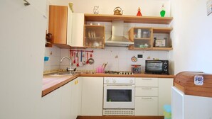 Cocina compacta con armarios blancos, cocina a gas, horno, tostadora y lavaplatos.