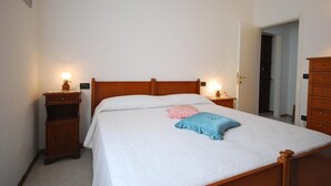 Una cama individual con ropa blanca, dos mesitas de noche con lámparas, un tocador de madera y un aparador de madera.