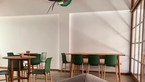 A spacious room with a high ceiling, wooden beams, a large window, and a green chair in the foreground. - La Maison Samaï (Urubamba)