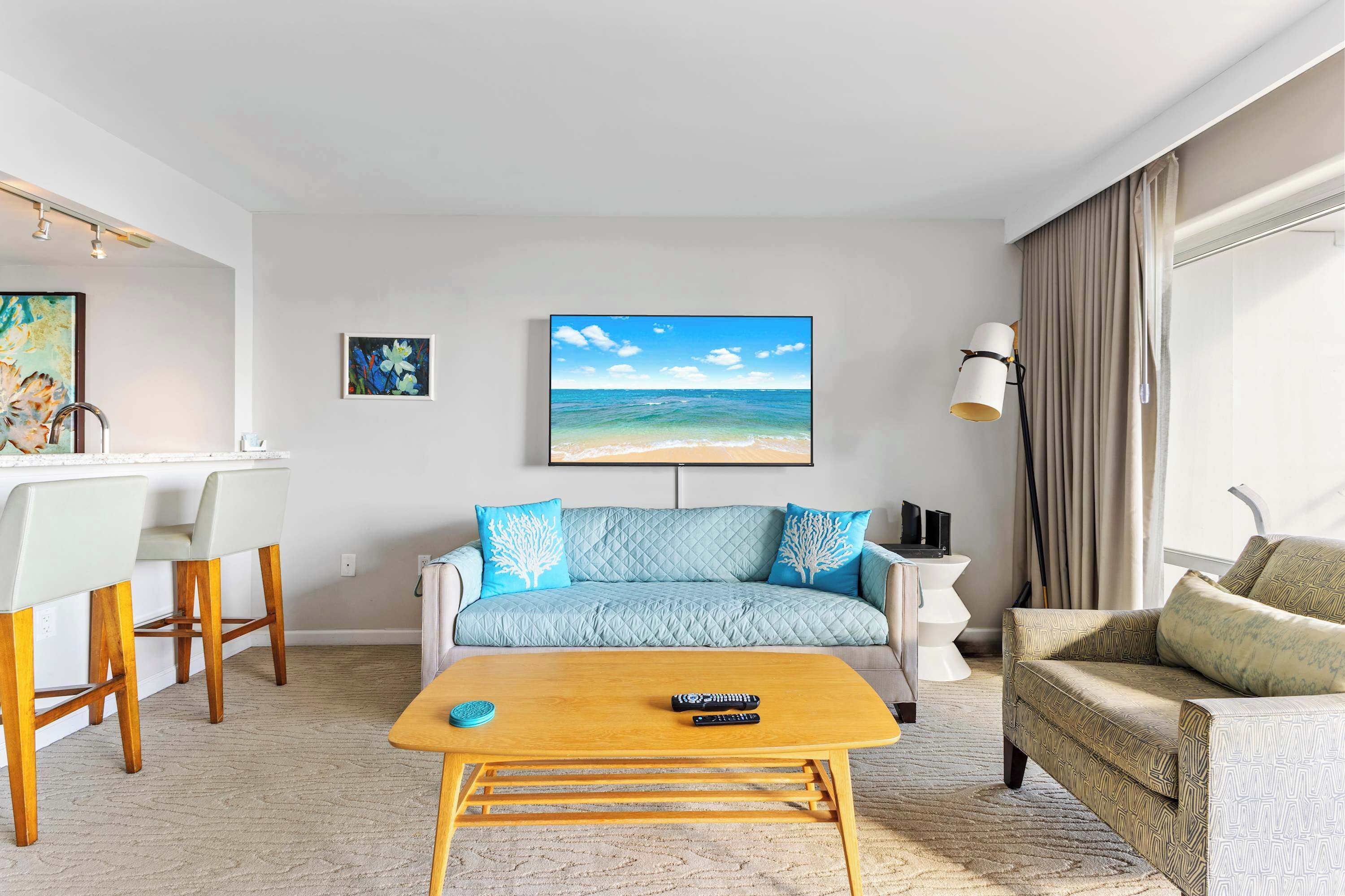 Una sala de estar con un sofá, una mesa de centro, un televisor y un cuadro de una escena de playa.