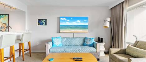 Una sala de estar con un sofá, una mesa de centro, un televisor y un cuadro de una escena de playa.
