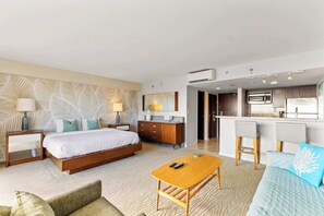 A modern hotel room with a bed, a wooden coffee table, a sofa, a desk, and a kitchenette.