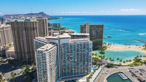 A high-rise hotel with multiple floors, a beach, and a clear view of the ocean.