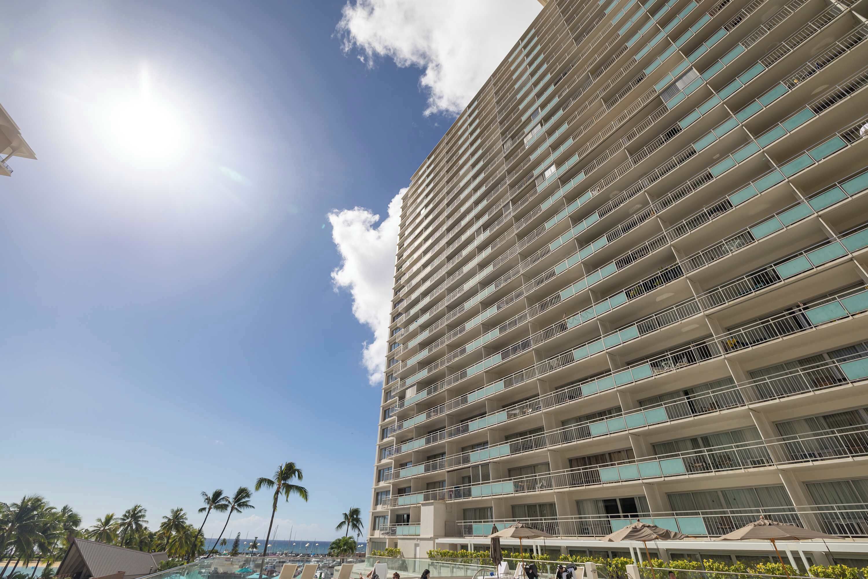 A high-rise hotel with multiple balconies, a pool area, and a view of the beach.