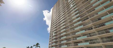 A high-rise hotel with multiple balconies, a pool area, and a view of the beach.