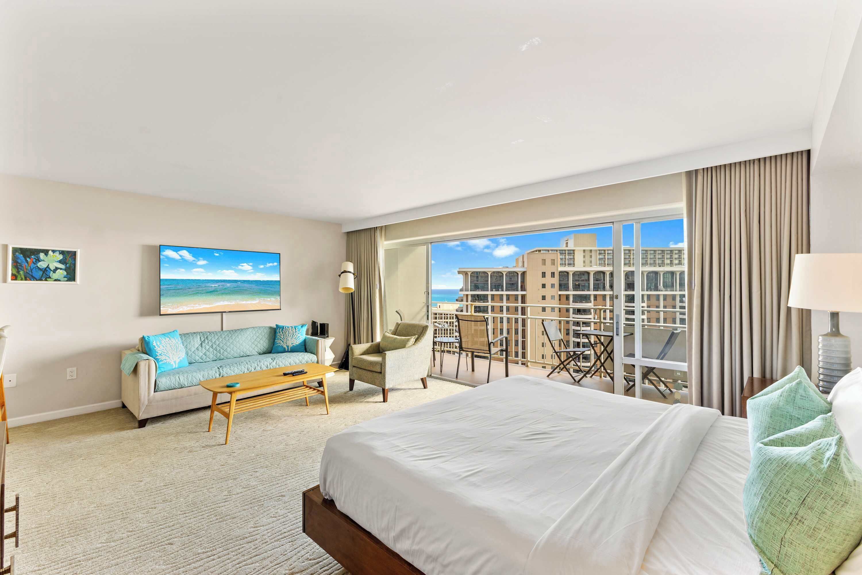 Een hotelkamer met een groot bed, een bank, een bijzettafeltje en een balkon met uitzicht op de stad.