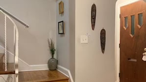 Una escalera con escalones de madera y barandilla blanca, que conduce a una habitación con una puerta de madera y un interruptor de luz en la pared.