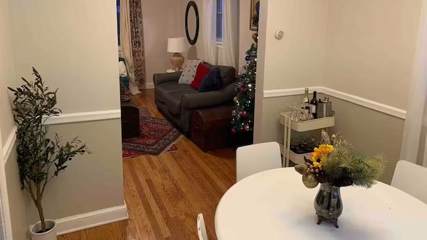 Una sala de estar con un sofá, un árbol de Navidad y una mesa de comedor con un florero.