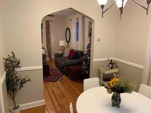 A living room with a sofa, a Christmas tree, and a dining table with a vase of flowers.