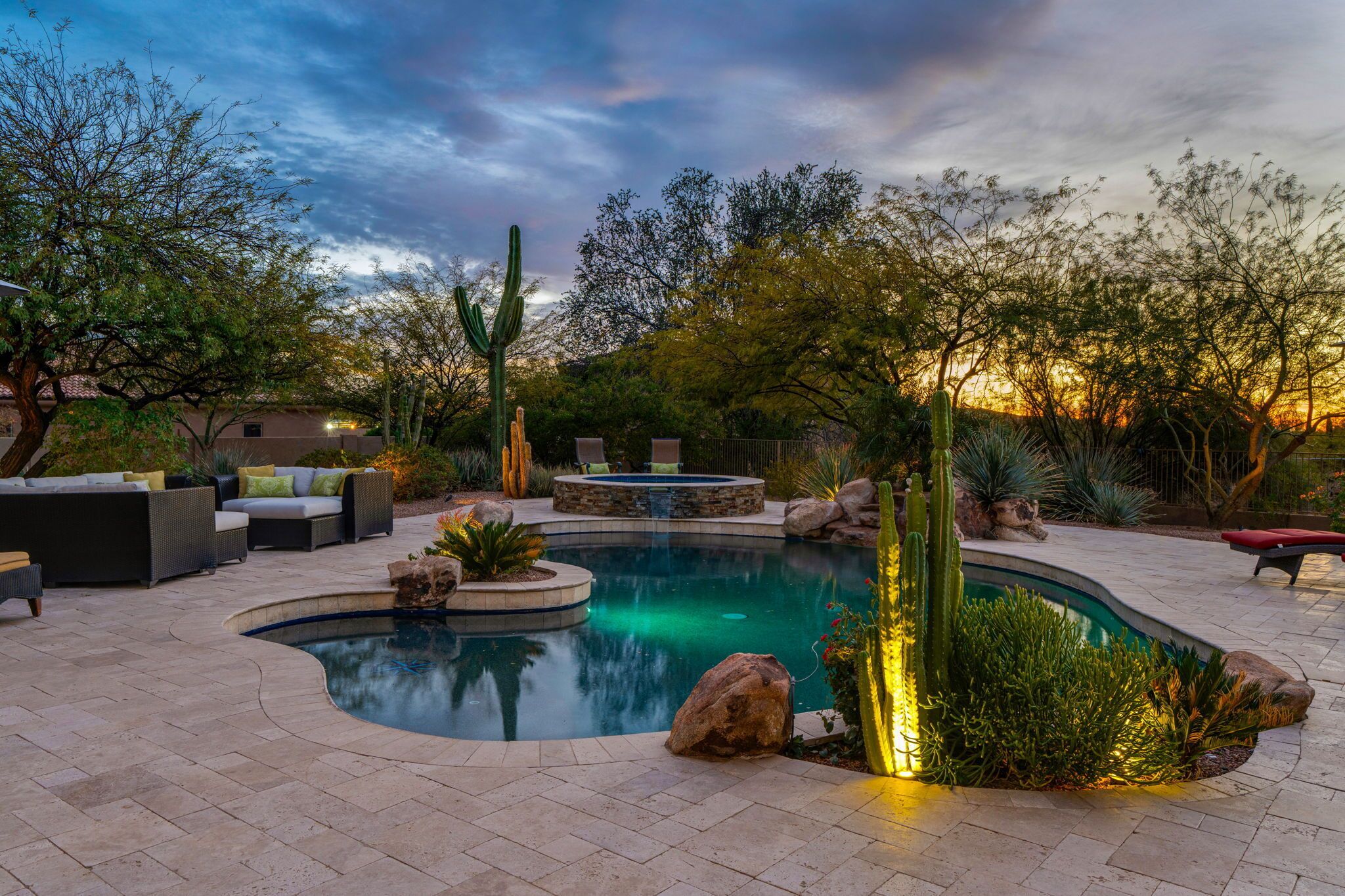 A landscaped outdoor area with a swimming pool, patio furniture, and cacti.