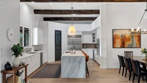 A modern kitchen with white cabinetry, a marble island, and a dining area with a wooden table and chairs. - NEW RENOVATION! A Modern Twist on Southwest Living (Scottsdale)