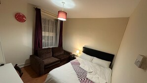 Une chambre d’hôtel de taille modeste, comprenant un lit simple, un petit canapé, un bureau et une fenêtre avec des rideaux.