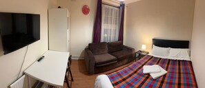 Une chambre d’hôtel avec un lit, un canapé, un bureau, une télévision et une fenêtre avec des rideaux.