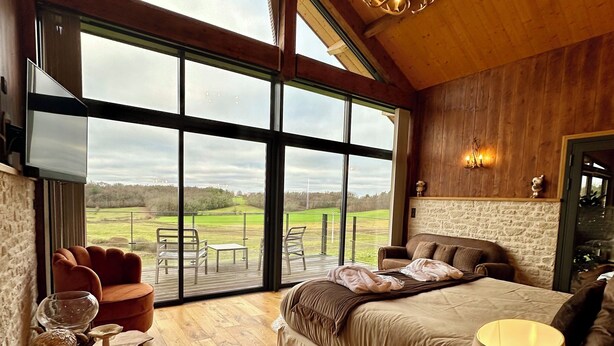 A spacious bedroom with a large window, a bed, a wooden table, and a chair. - L'Orée du Bois du Domaine des Hauts de Rouquette (Eymet)