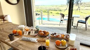 A breakfast table with croissants, orange juice, and a view of a pool and landscape. - L'Orée du Bois du Domaine des Hauts de Rouquette (Eymet)