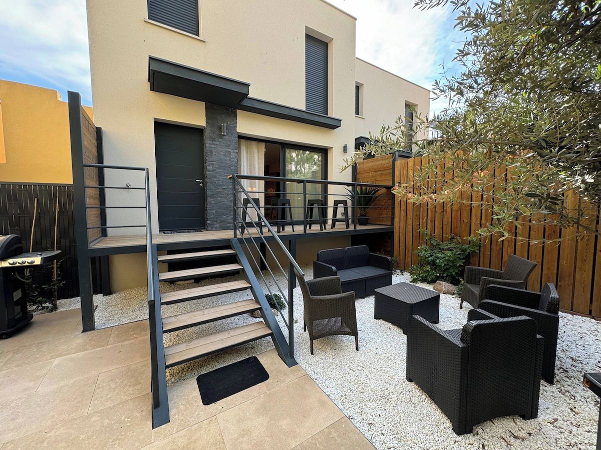 A modern outdoor patio with a staircase leading to a deck, surrounded by outdoor furniture and a wooden fence.