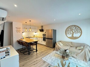A modern kitchen with a dining area, a sofa, and a decorative wall piece. - Villa Paradis 2 Sun Sea and Beach (Valras-Plage)