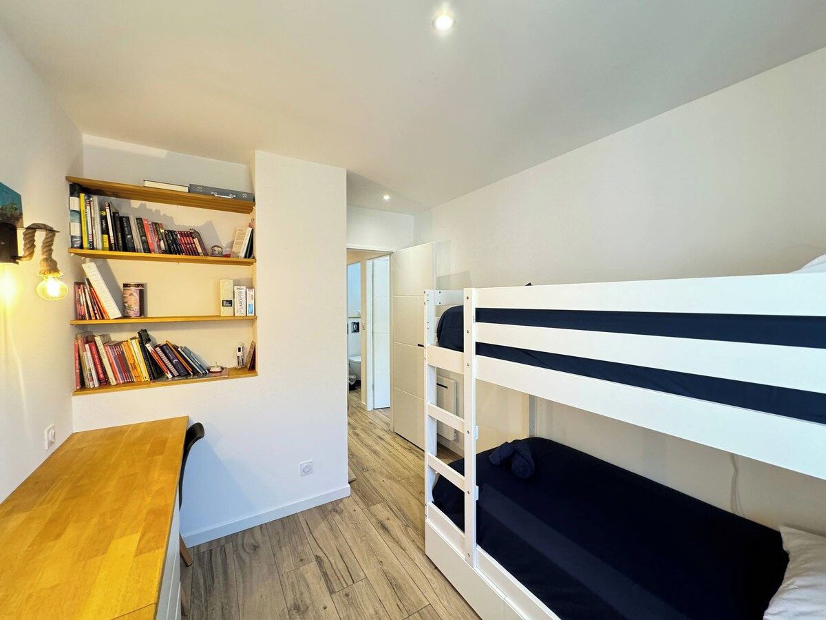 A compact room with a bunk bed, a wooden desk with a chair, and a bookshelf.