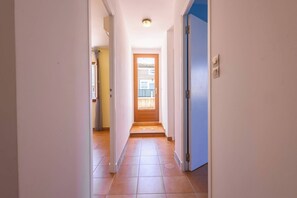 Un pasillo que conduce a una puerta con ventana, suelo de baldosas e iluminación en el techo.