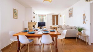 A dining area with a wooden table, white chairs, and a television. - Village House near the Canal (Colombiers)