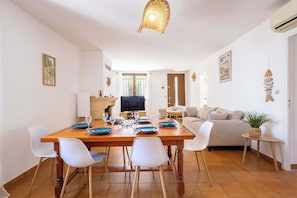 Un coin repas avec une table en bois, des chaises blanches et un téléviseur.