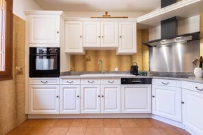 A kitchen with white cabinets, a stainless steel range hood, a dishwasher, and a black oven. - Village House near the Canal (Colombiers)
