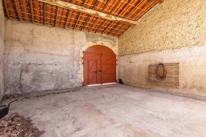 A room with a concrete floor, a wooden ceiling, a large arched doorway, and a wall-mounted basket. - Village House near the Canal (Colombiers)