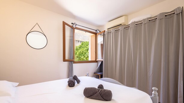Habitación de hotel con cama, un espejo redondo, una ventana con cortinas y un equipo de aire acondicionado.