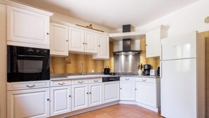 Una cocina con armarios blancos, una campana extractora de acero inoxidable, lavavajillas y refrigerador.