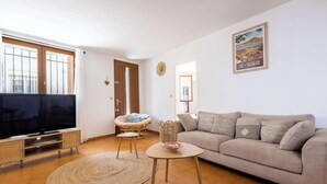 Una sala de estar con televisor, sofá, sillón de mimbre y un cartel en la pared.