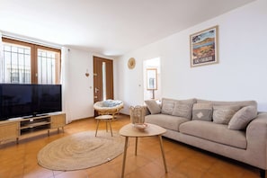 A living room with a TV, sofa, wicker chair, and a wall with a poster. - Village House near the Canal (Colombiers)