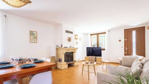 Una sala de estar con chimenea, televisor, sofá y comedor con mesa lista para cuatro.