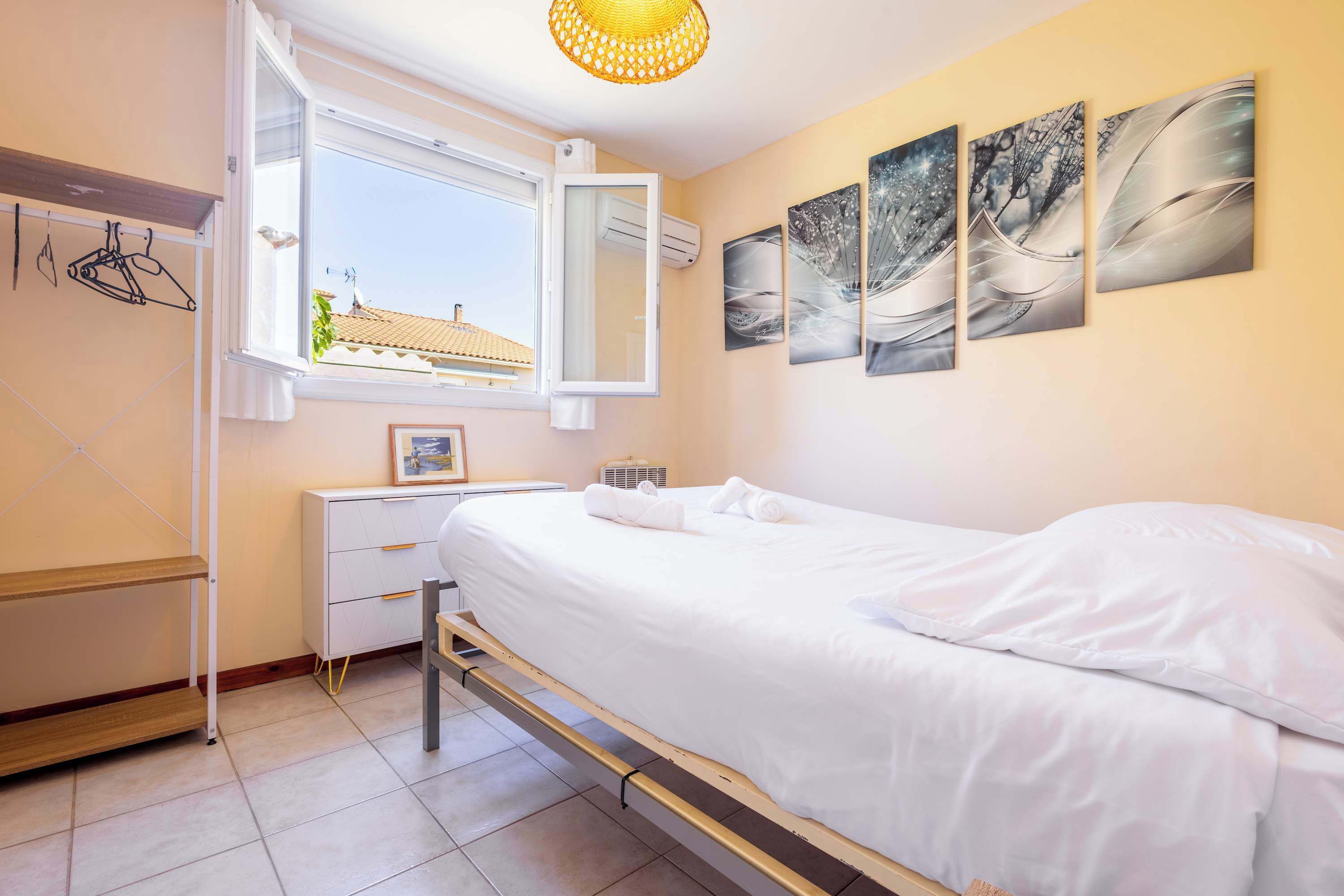 A bedroom with a bed, a bedside table, a window, and wall art.