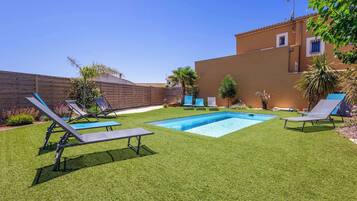 A backyard with a swimming pool, two lounge chairs, and a wooden fence.