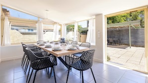 A dining area with a wooden table and black chairs, large windows, and a view of the backyard. - Villa Familiale avec Piscine et Petanque (Valras-Plage)
