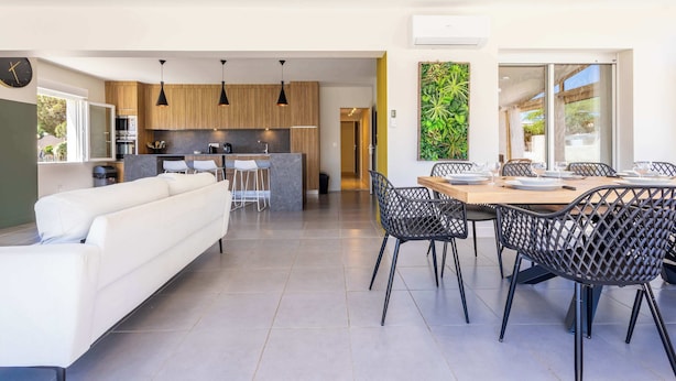 A modern kitchen with wooden cabinets, a dining area with a table and chairs, and a living room with a sofa. - Villa Familiale avec Piscine et Petanque (Valras-Plage)