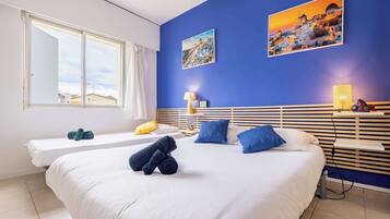 Een hotelkamer met een groot bed, een kleiner bed, een raam met gordijnen, een wandlamp en twee schilderijen.