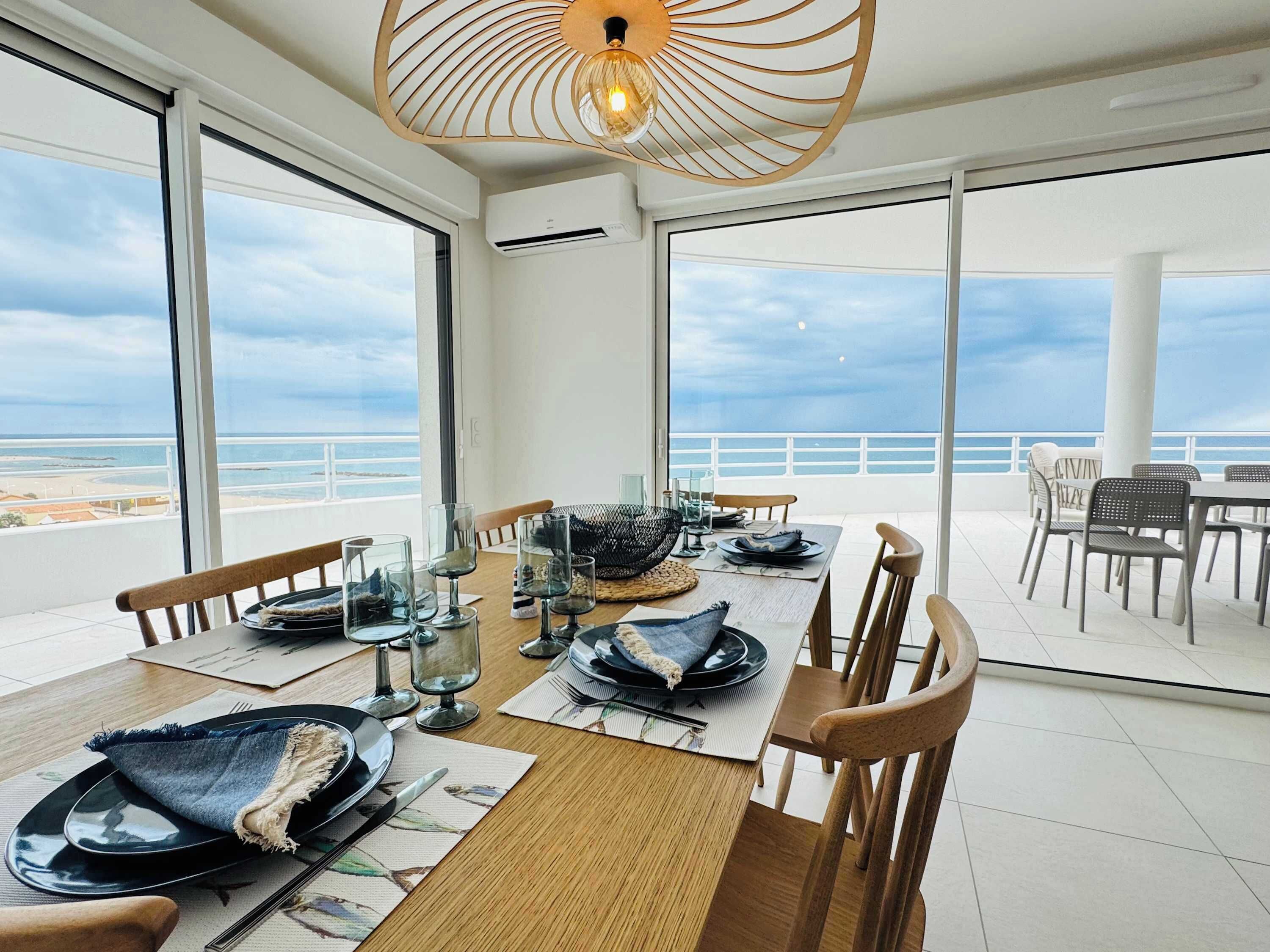 A dining area with a table set for four, overlooking a beach.