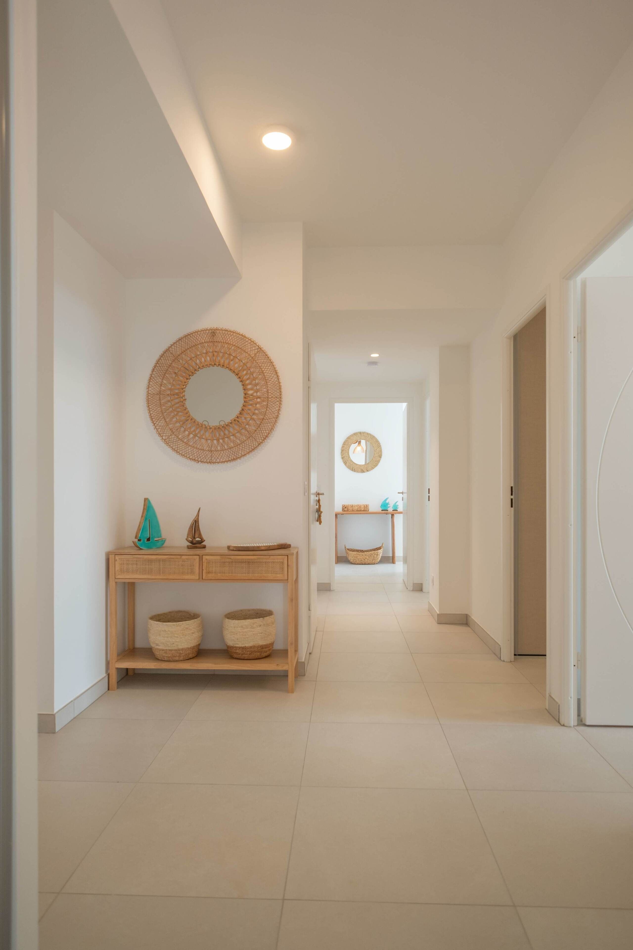 Un pasillo con una consola de madera, cestas de mimbre y dos espejos colgados en la pared.