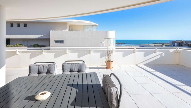 A rooftop terrace with a table and chairs, a potted plant, and a view of the sea.