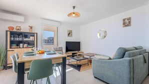 A modern living room with a dining area, a sofa, a TV, and a large window.