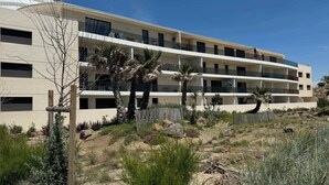 A multi-story hotel with balconies, surrounded by desert vegetation and a wooden fence. - Valras'Loc Archipel Capri Balcony over the Sea (Valras-Plage)