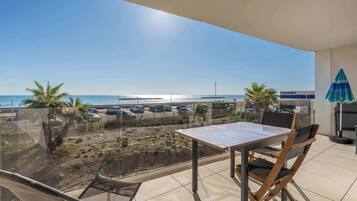 Een balkon met een tafel en stoelen, uitkijkend op een strand met geparkeerde auto's en een bord van een casino.