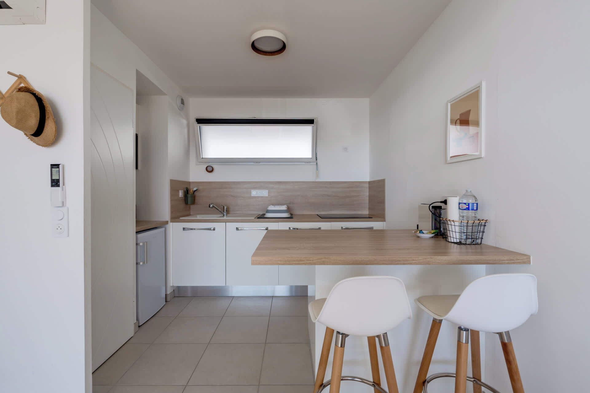 A modern kitchen with a wooden countertop, white cabinets, and two white bar stools.
