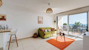 A modern living room with a green sofa, white chairs, a small table, and a large window offering a view of the sea. - Valras'Loc Archipel Capri Balcony over the Sea (Valras-Plage)
